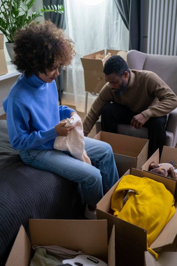 a-woman-sitting-in-front-of-a-cardboard-box-with-clothes-holding-a-white-fabric-6612093 A Woman Sitting in Front of a Cardboard Box with Clothes Holding a White Fabric